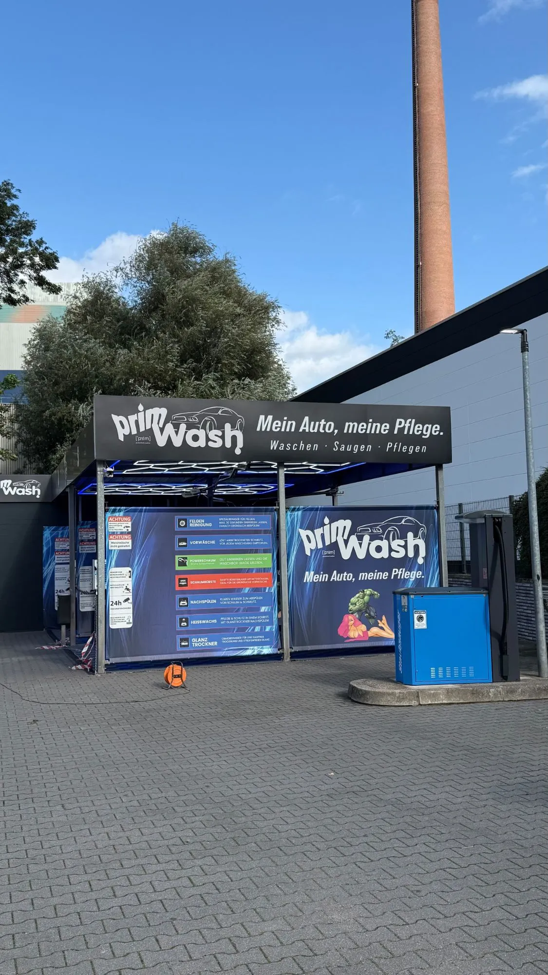 Außenansicht des neuen Prim Wash Standorts an der Gladbecker Straße bei Tag: Schild „Mein Auto, meine Pflege“ über den Waschboxen, davor eine blaue Sauger-Station